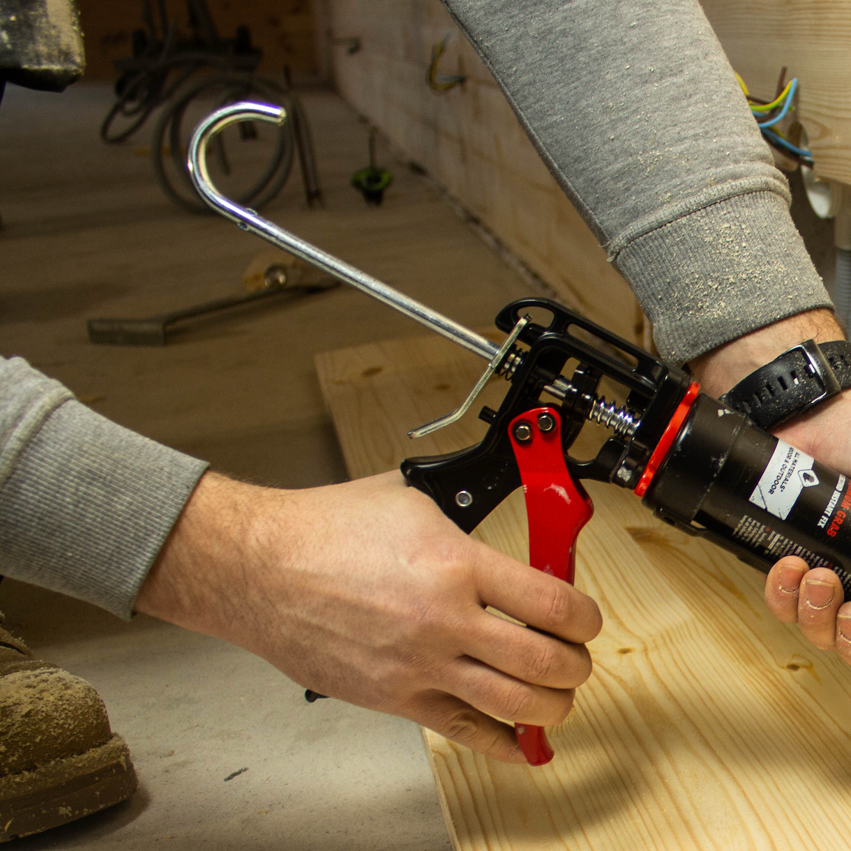 Person using a caulking gun on a wooden surface with tools in the background